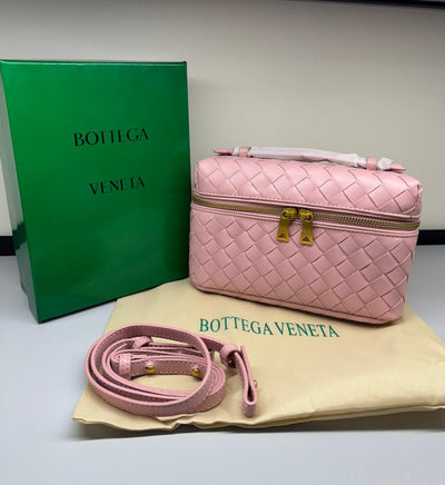 Pink Bot tega Ven eta handbag with matching strap on a beige mat, with green box in the background.