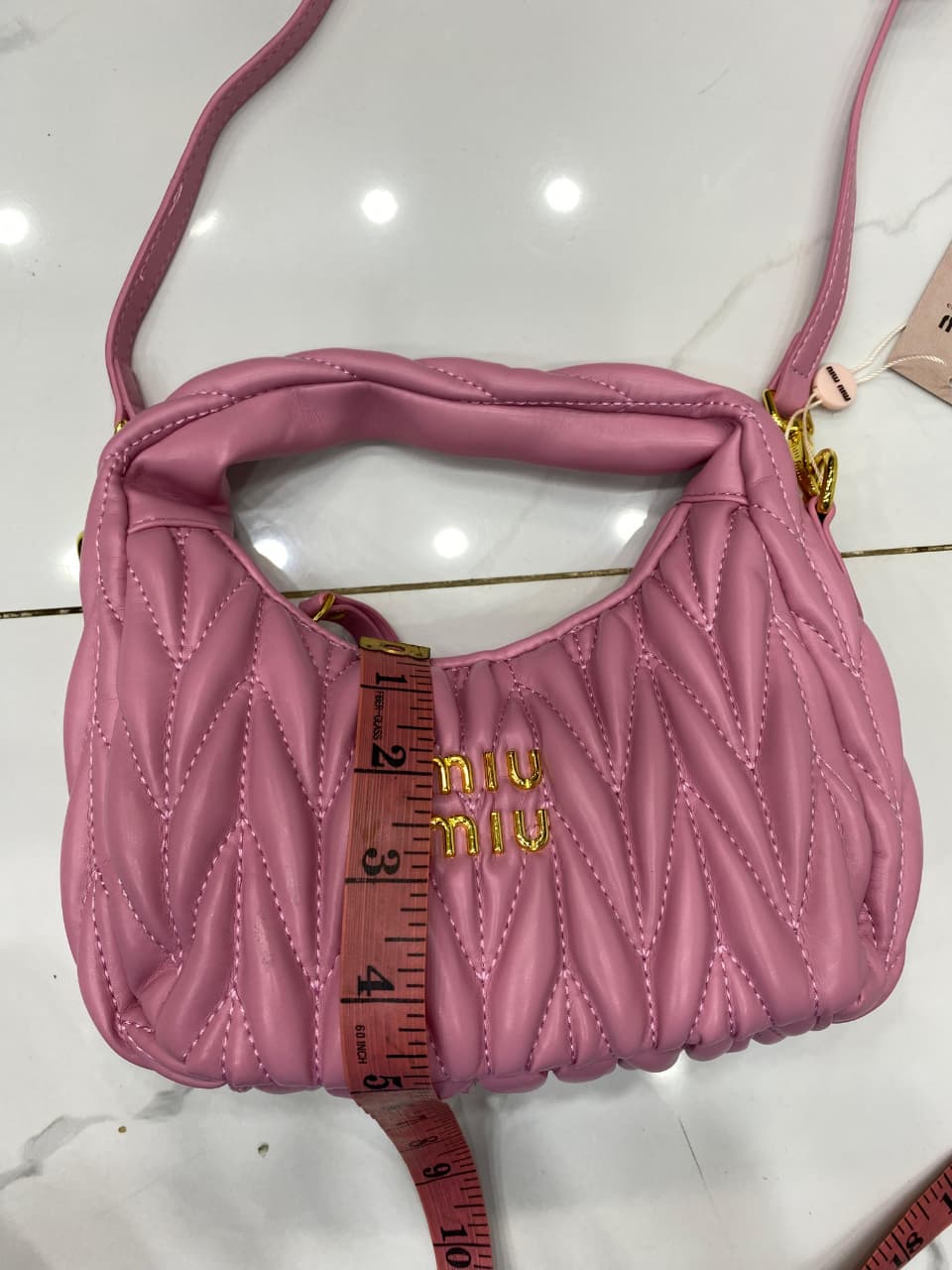 Pink handbag with 'MI-U MI-U' branding on a white surface.