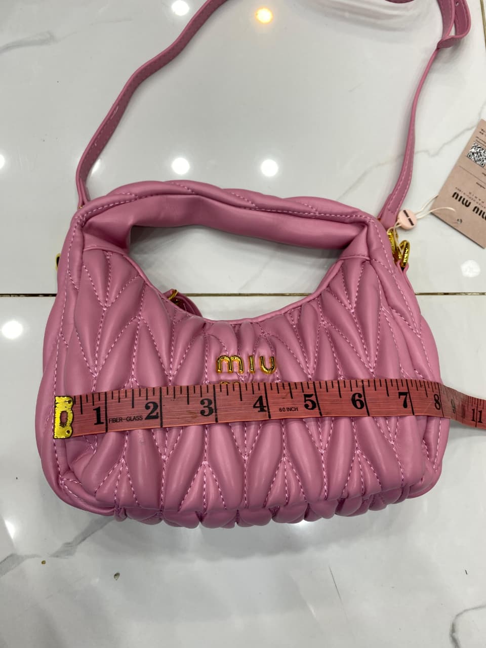 Pink handbag with 'Mi u Mi u' logo being measured with a tape measure on a white background.