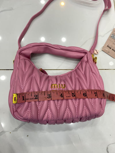 Pink handbag with 'Mi u Mi u' logo being measured with a tape measure on a white background.