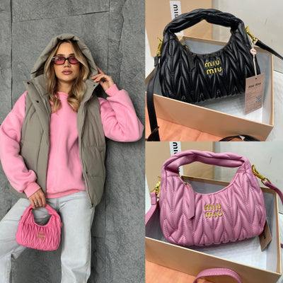 Person wearing pink hoodie and gray vest holding a pink Mi-u Mi-u handbag, with black and pink Mi-u Mi-u handbags in boxes.