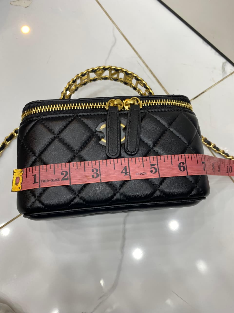 Black quilted handbag with gold chain strap on a light tiled floor.