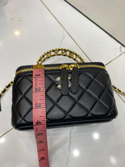 Black quilted handbag with gold chain and zipper, measured with a red tape measure on a white background.