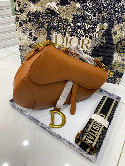Brown saddle-shaped handbag with gold accents on a Di or branded surface