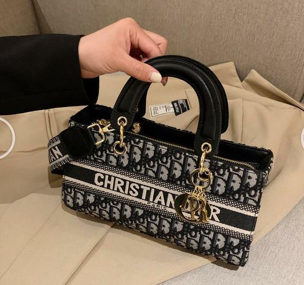 Black and white patterned handbag with gold hardware held by a hand on a beige surface.