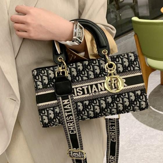 Designer handbag with visible brand logo held by a person in a beige outfit.