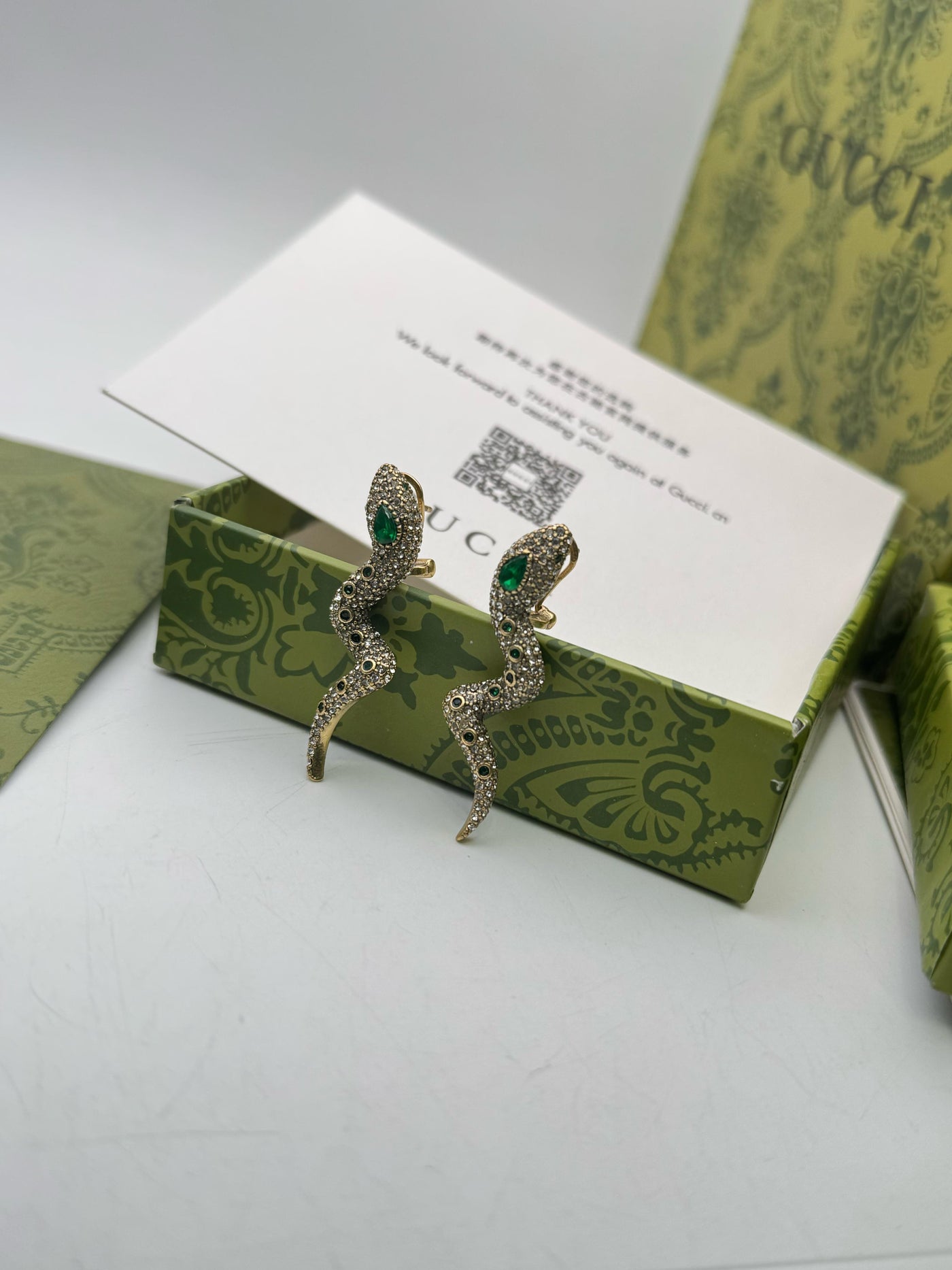 Pair of Guc-ci earrings on a green box with a card in the background
