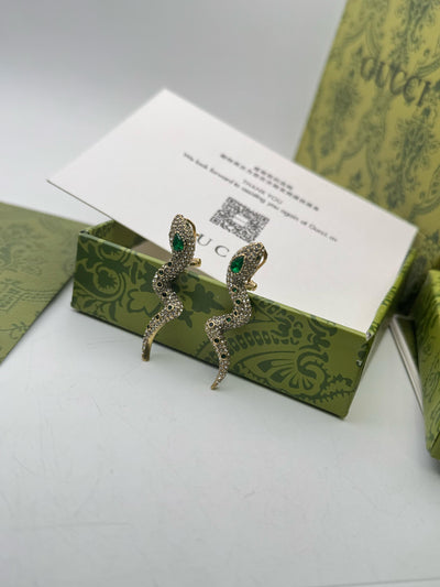 Pair of Guc-ci earrings on a green box with a card in the background
