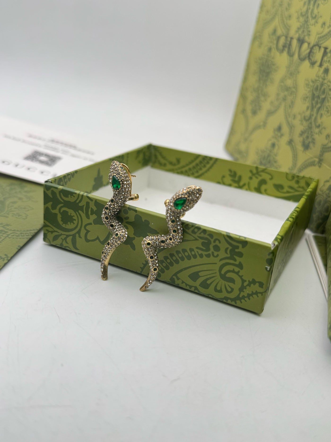 Pair of earrings with green gemstones in a decorative box on a white background