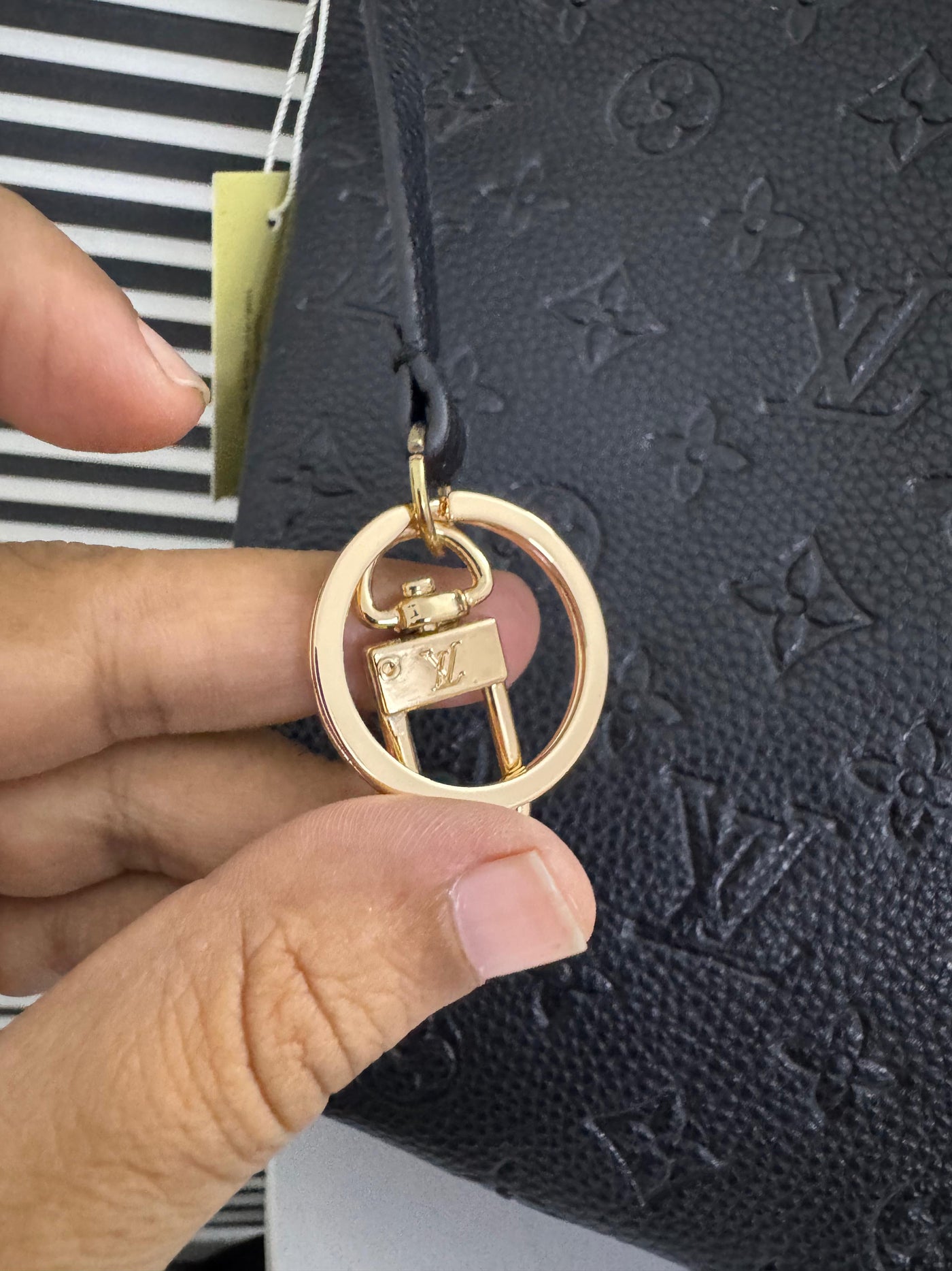 Gold keychain with a logo held in front of a black textured surface