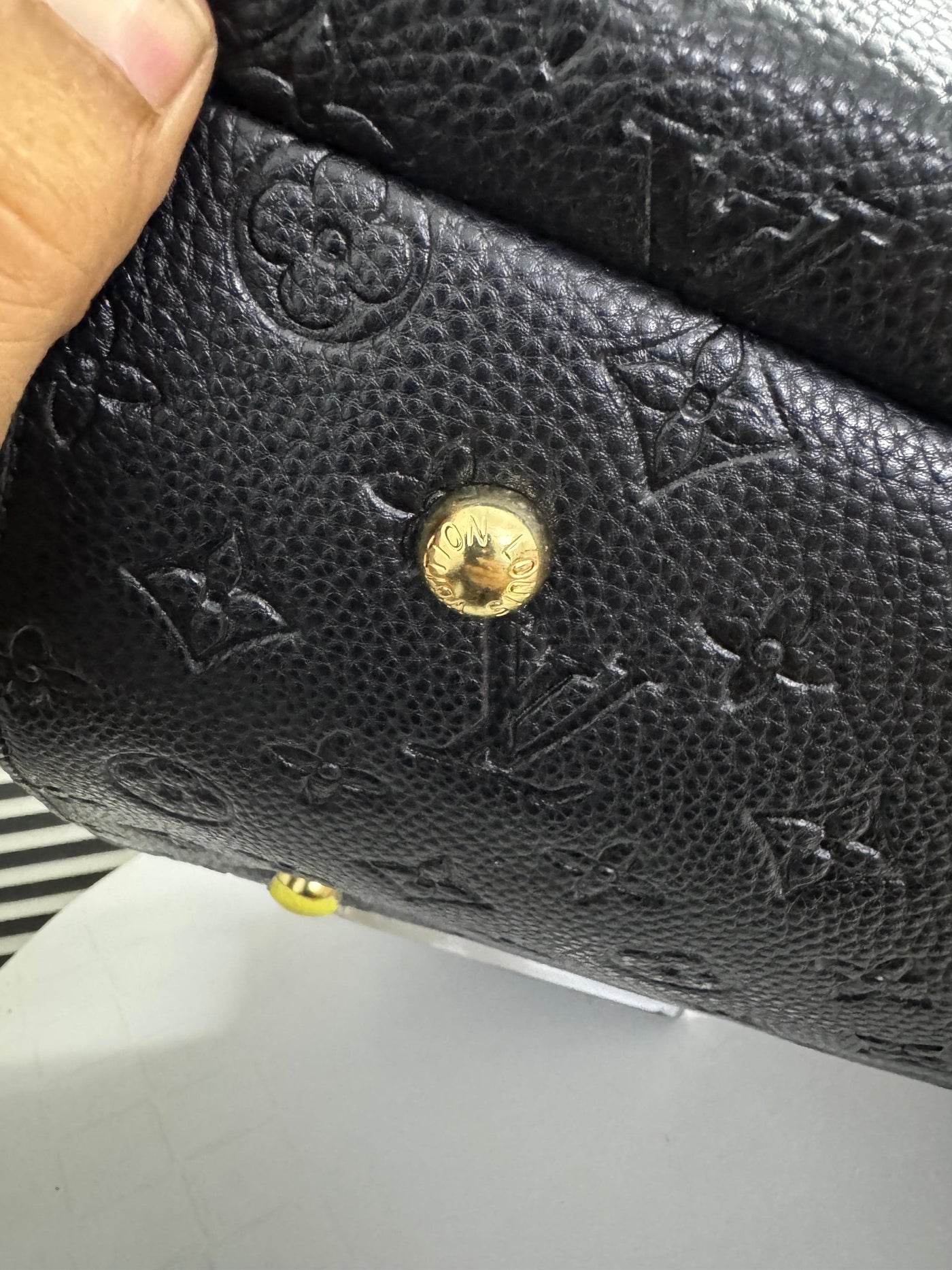 Close-up of a black textured wallet with a gold button, held by a hand.