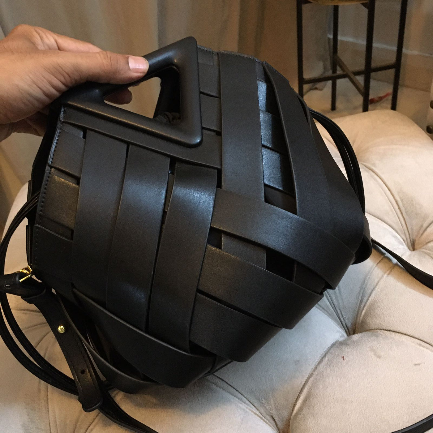 Black woven leather backpack held by a hand on a light-colored couch.