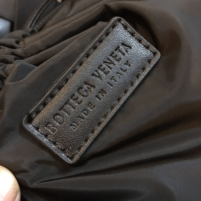 Close-up of a label on a dark fabric, likely a garment, with 'Bott-ega Ven-eta' branding.
