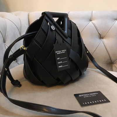 Black woven handbag with tags on a light gray cushioned surface