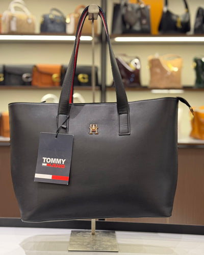 Gray handbag with a Tom my Hil figer tag on a stand in a store setting.