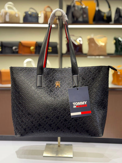 Black woven handbag with Tom my Hil figer tag on a stand against a blurred background of other bags.