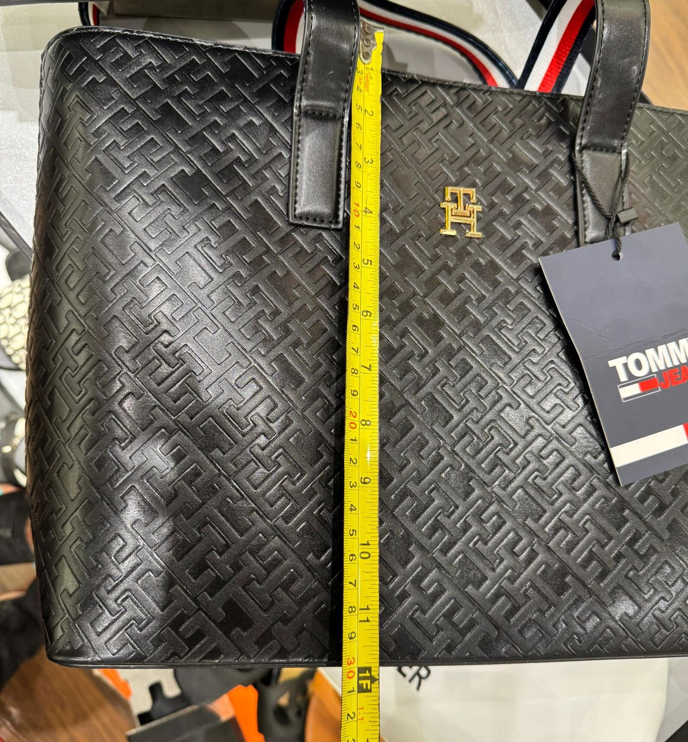 Black textured bag with a measuring tape for scale, featuring a brand tag.