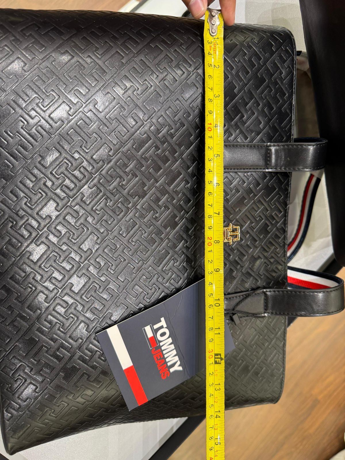 Black textured bag with a measuring tape and Tom my Hil figer tag