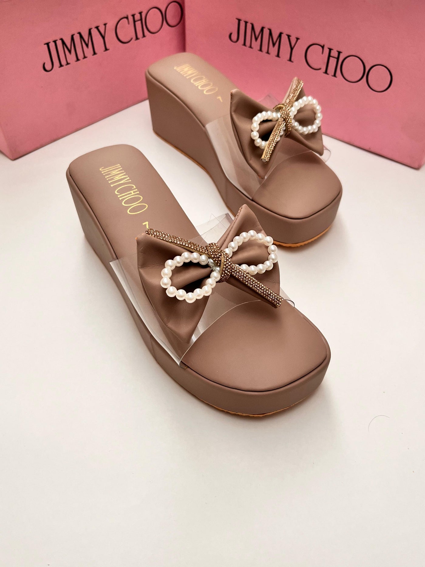 Brown wedge sandals with decorative bows on a white surface, with 'Jim my Ch oo' branding.