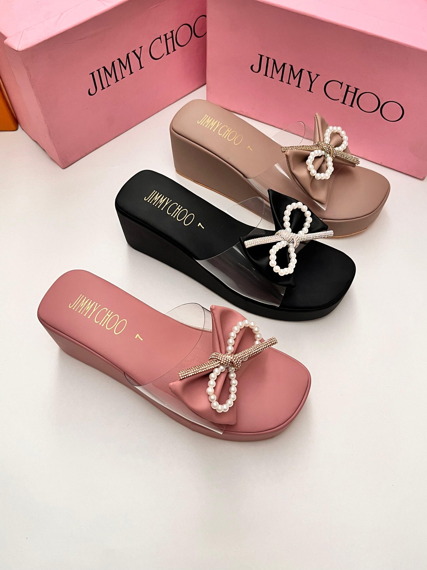 Jimmy Choo sandals in black, pink, and beige with pearl embellishments on a white background.