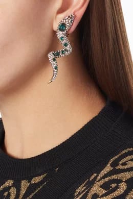 Close-up of a person wearing a decorative earring with green gemstones.