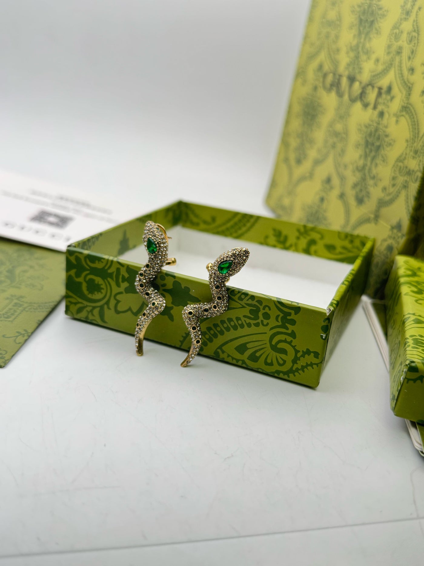 Pair of earrings with green stones in a Guc-ci box on a white background